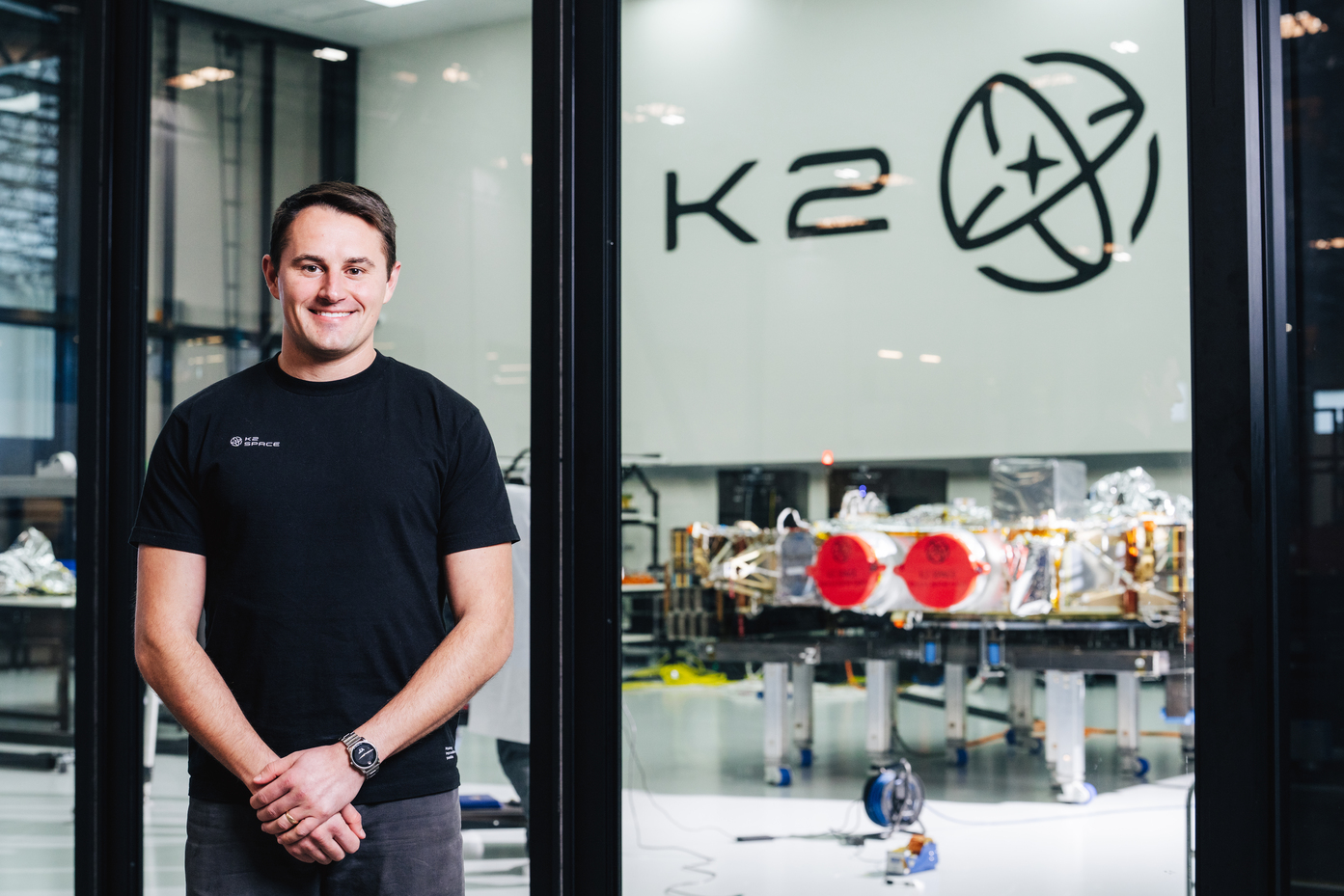 Mitchell posing in front of a satellite. The wall behind him reads "K2".